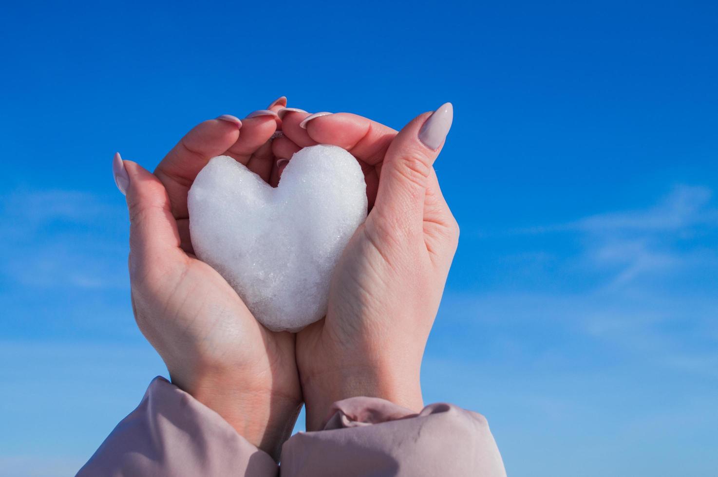 mani femminili con cuore bianco dalla neve nella giornata invernale foto