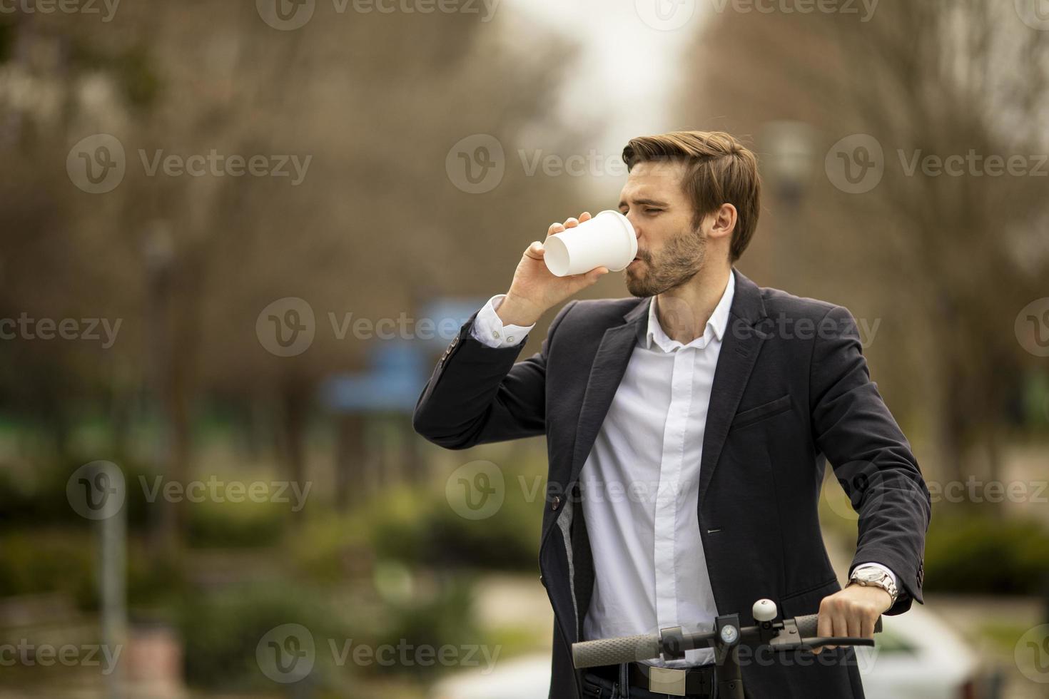 giovane imprenditore bere da asporto tazza di caffè su scooter elettrico foto