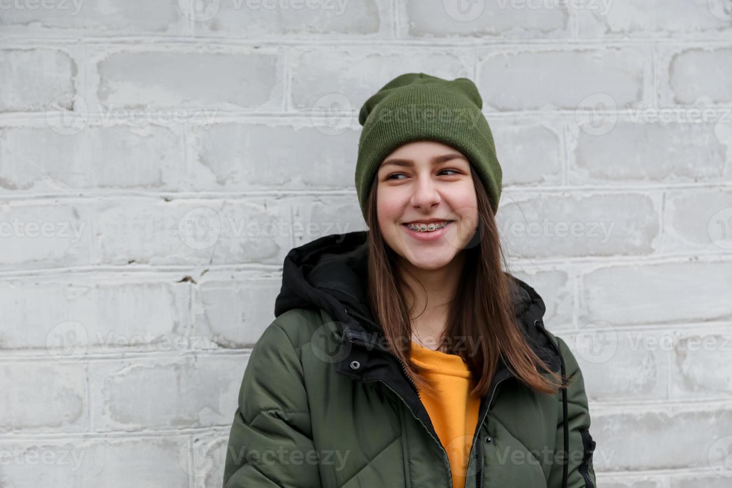 ritratto di una bella ragazza sorridente con le parentesi graffe in un maglione giallo e un cappello cachi foto