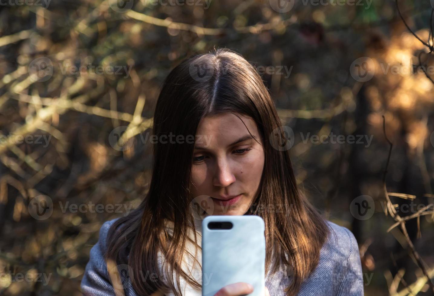 ragazza in un cappotto grigio prende un selfie nella foresta foto