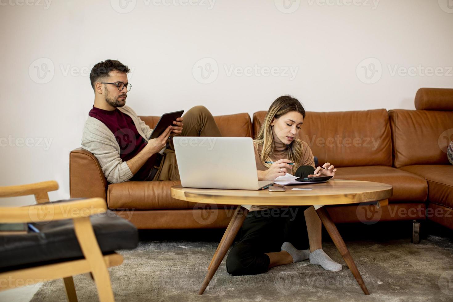 giovane donna e giovane uomo utilizzando laptop mentre è seduto dal divano di casa foto