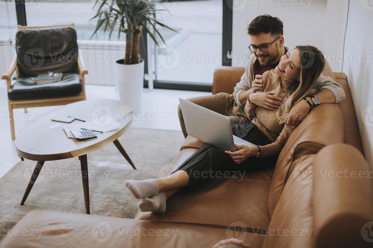 giovane coppia utilizzando laptop insieme mentre è seduto sul divano di casa foto