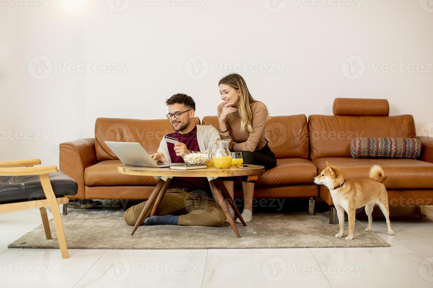 giovane donna e giovane uomo che utilizza il laptop per il pagamento online mentre è seduto sul divano con il loro cane Shiba Inu a casa foto