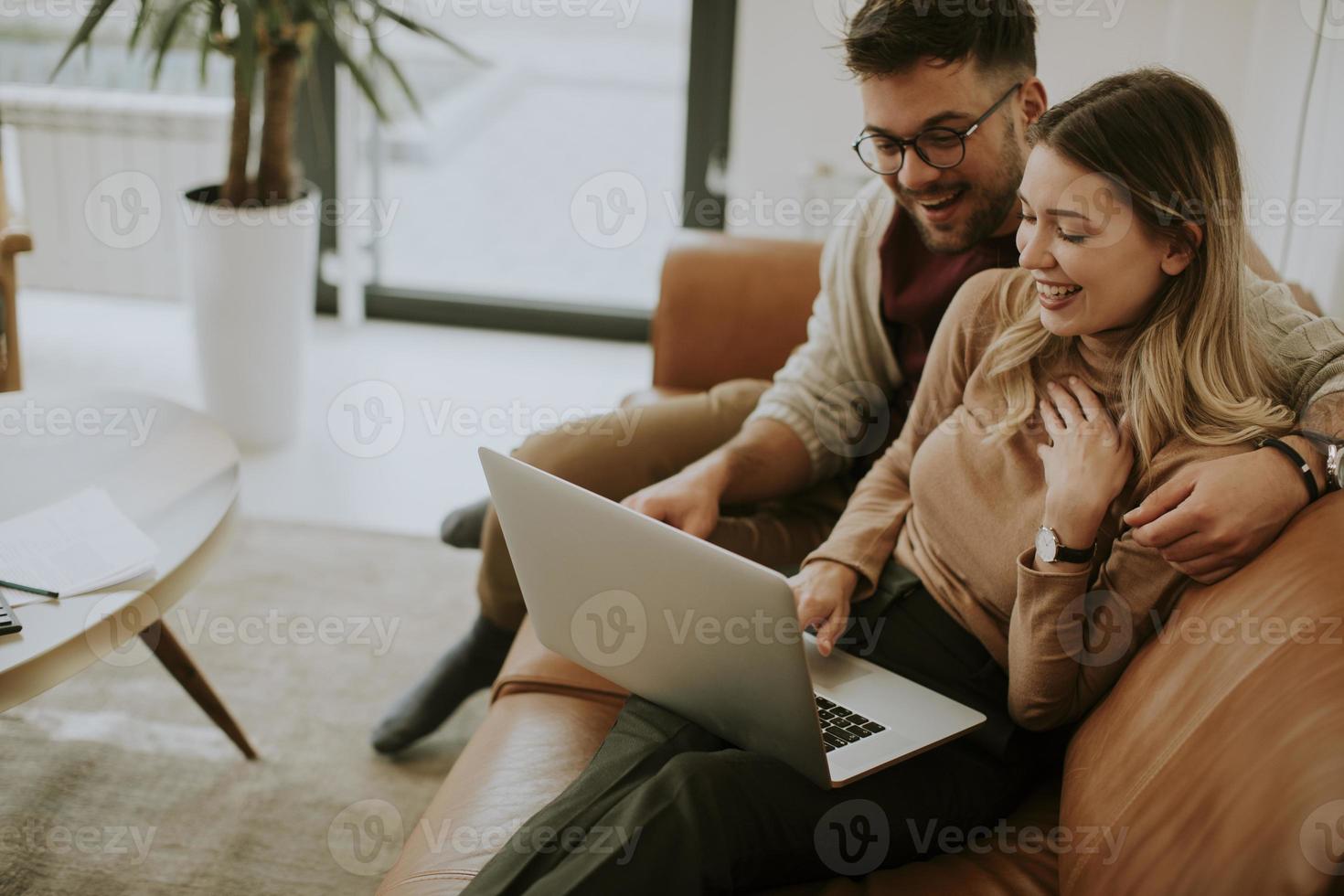 giovane coppia utilizzando laptop insieme mentre è seduto sul divano di casa foto