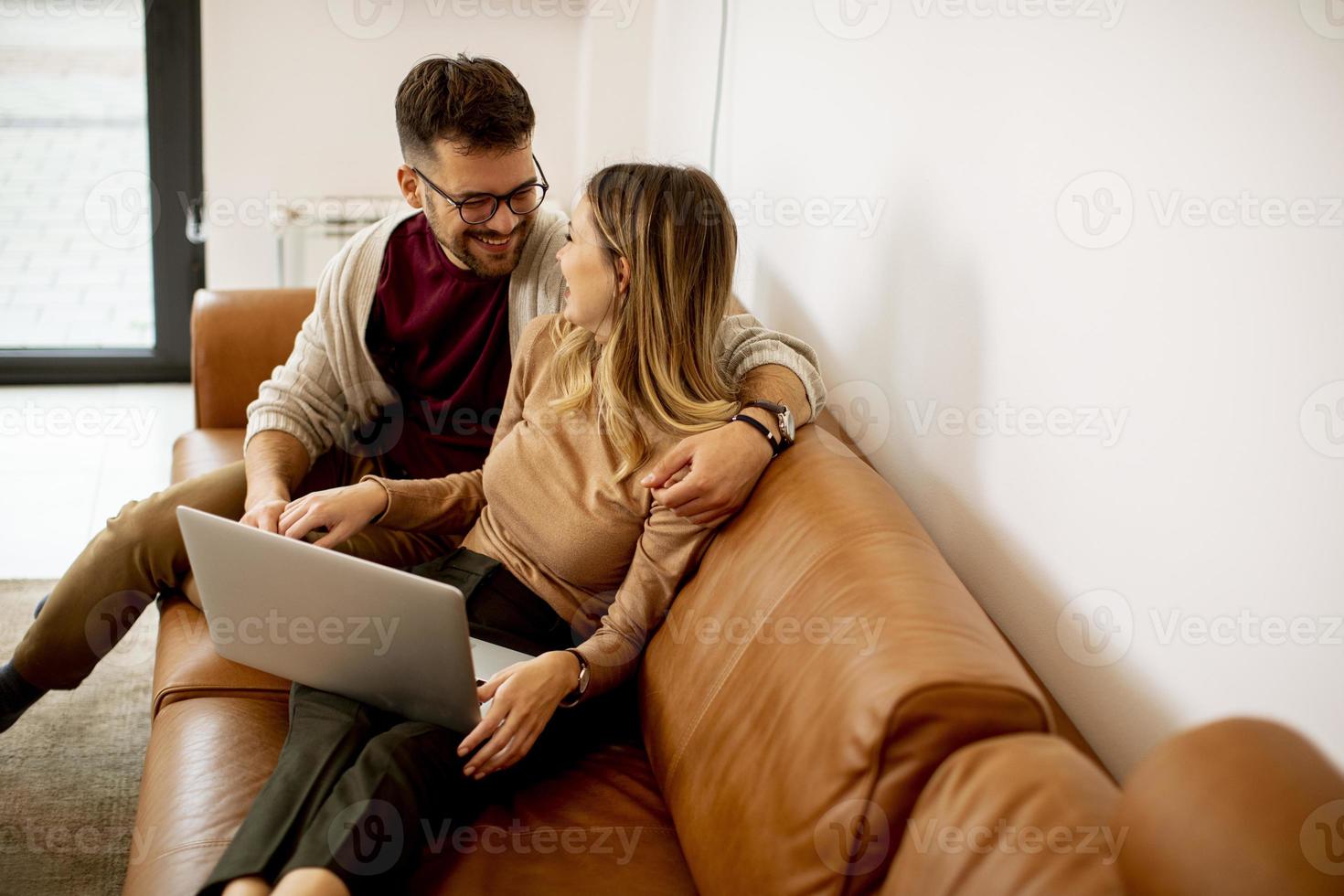 giovane coppia utilizzando laptop insieme mentre è seduto sul divano di casa foto