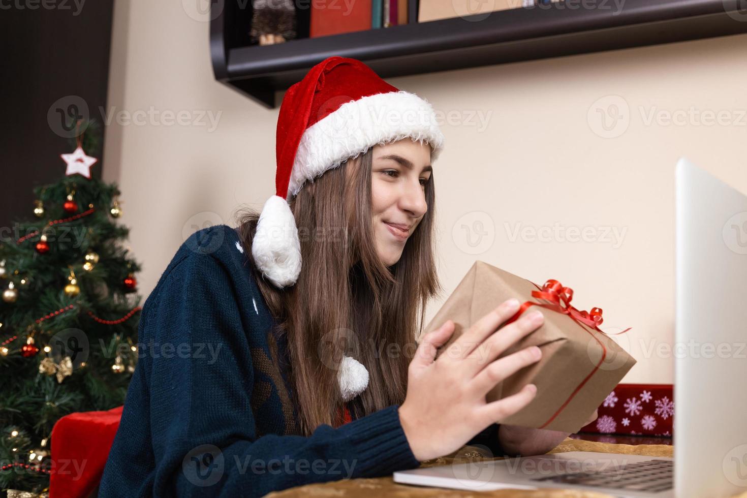 ragazza in cappello di Babbo Natale utilizzando laptop per videochiamata ad amici e genitori foto