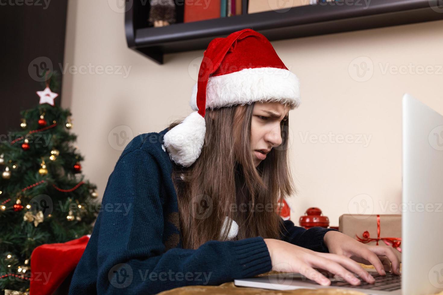 ragazza in cappello di Babbo Natale utilizzando laptop per videochiamata ad amici e genitori foto