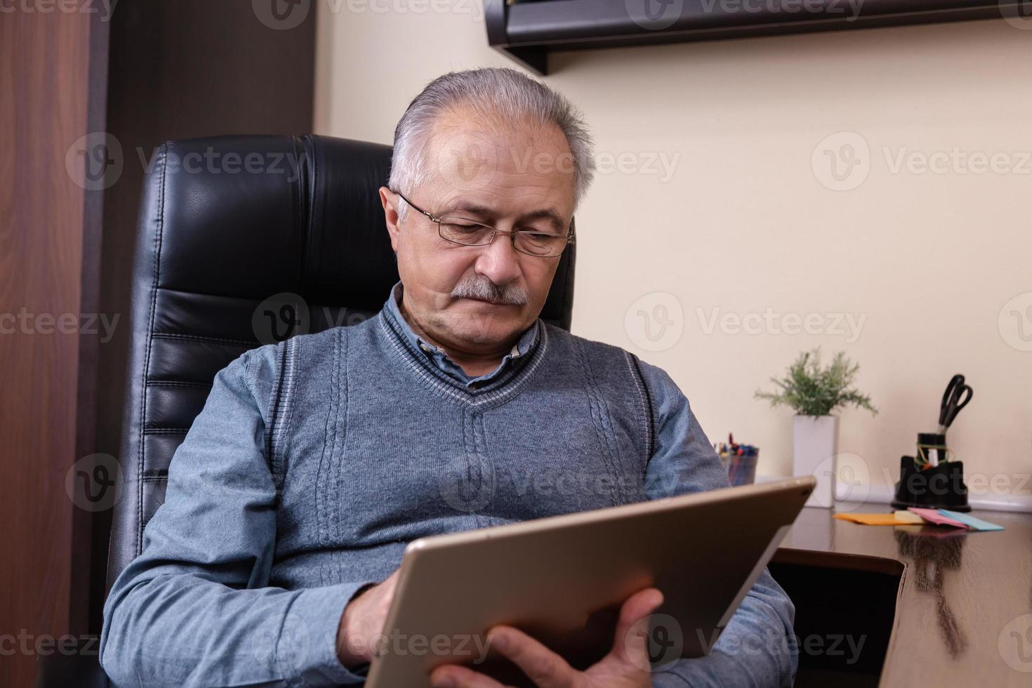 uomo anziano leggendo notizie sulla tavoletta digitale foto