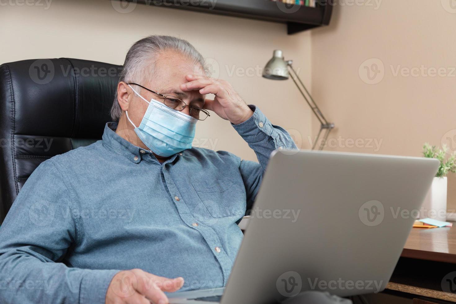 uomo anziano in maschera facciale lavorando o comunicando sul computer portatile a casa foto