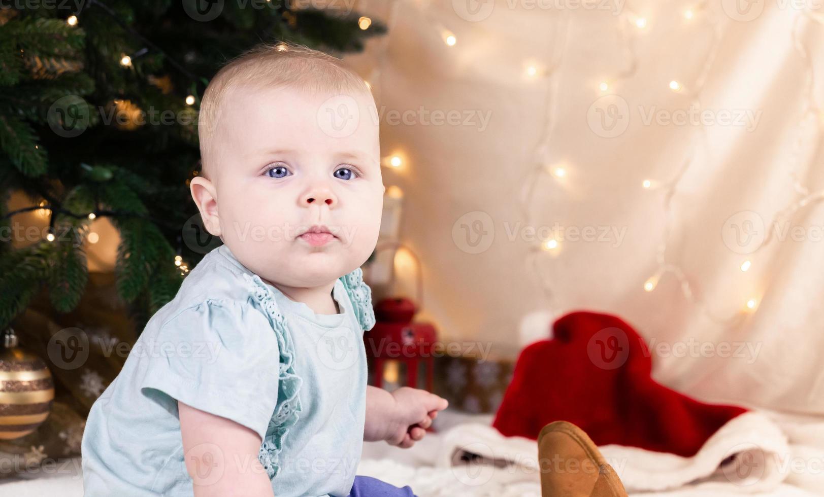 bambino in jeans e scarpe si siede vicino a un albero di natale foto