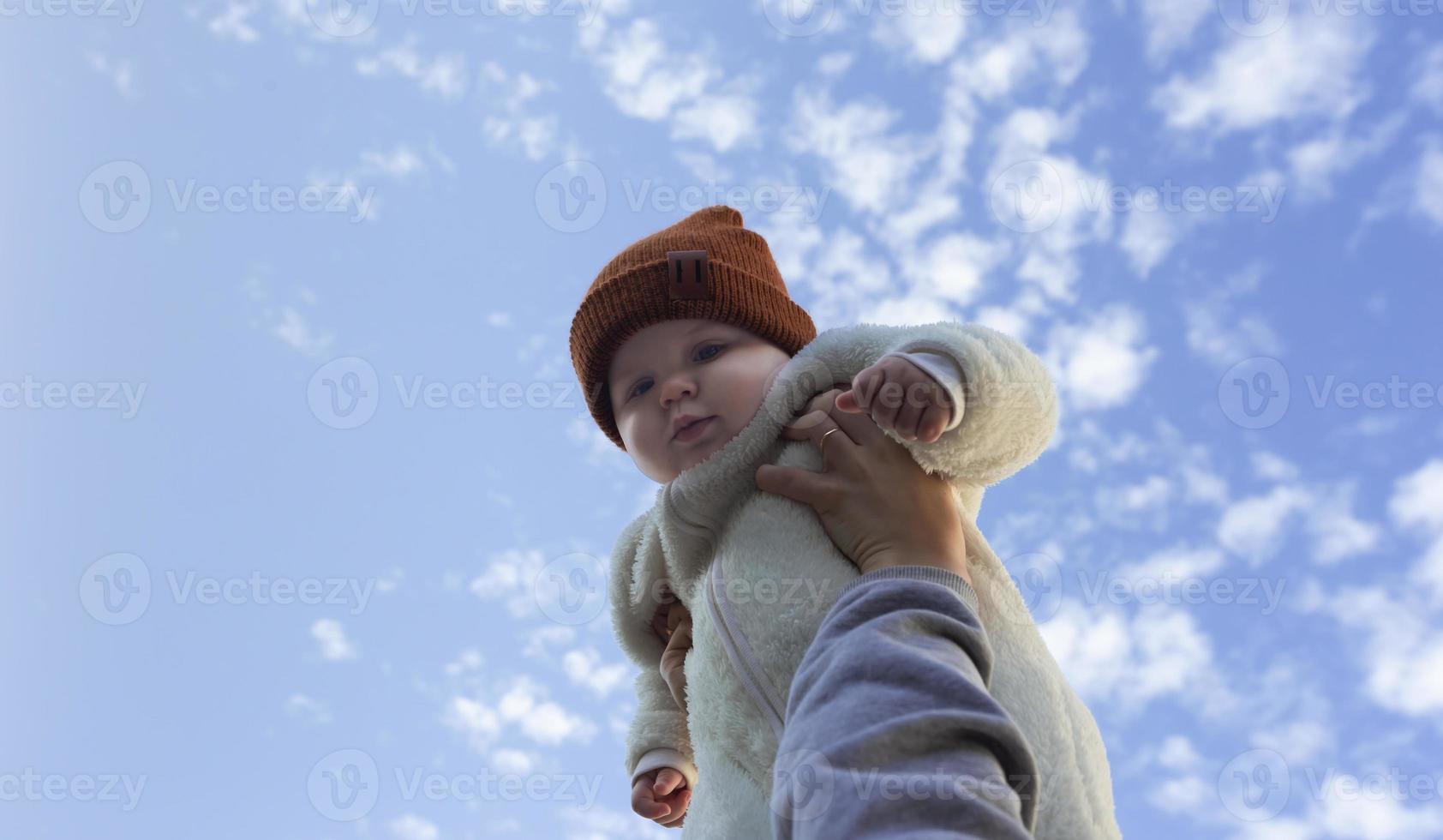 mani tagliate del genitore che tiene la figlia allegra del bambino contro il cielo blu foto