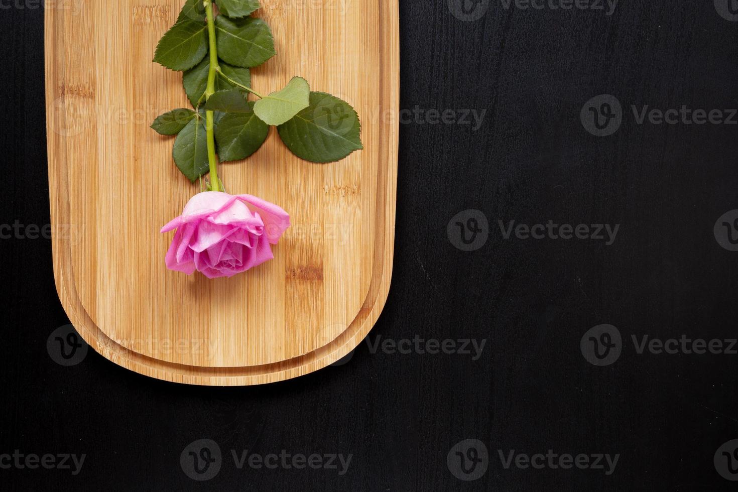 una rosa rosa giace su un tagliere di legno su uno sfondo scuro vista dall'alto con area per il testo foto