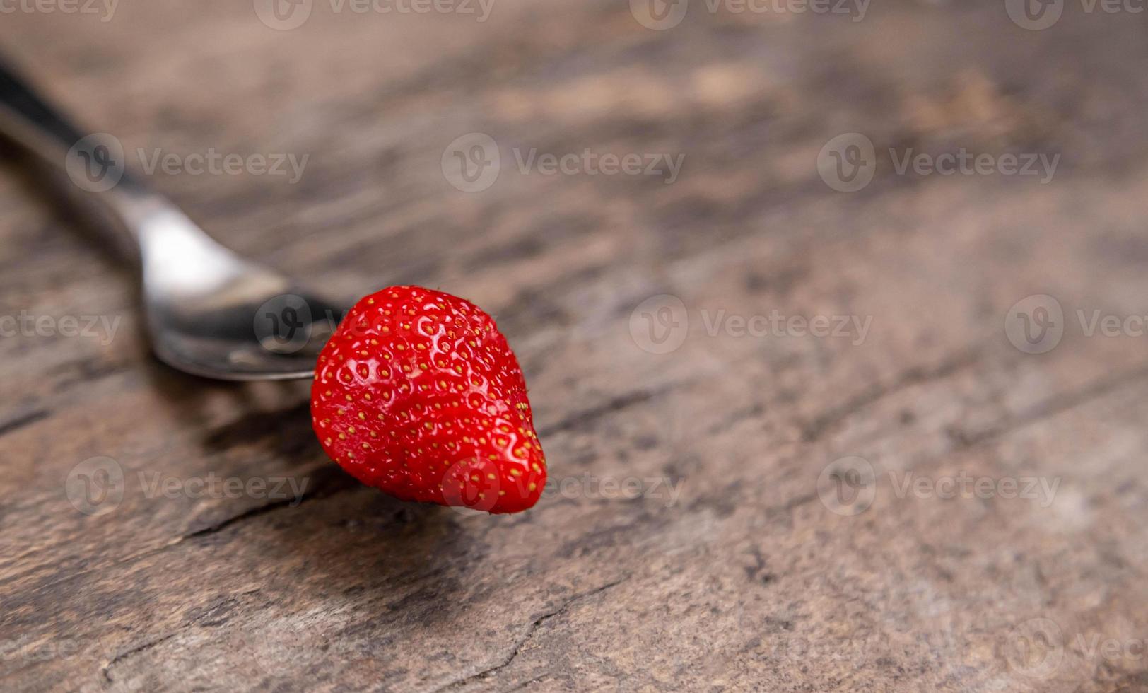 una fragola sulla forcella dorata su sfondo di vernice in legno non foto