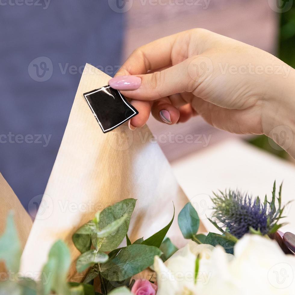 fioraio donna che fa di un bouquet di fiori e mettendo adesivo logo posto foto