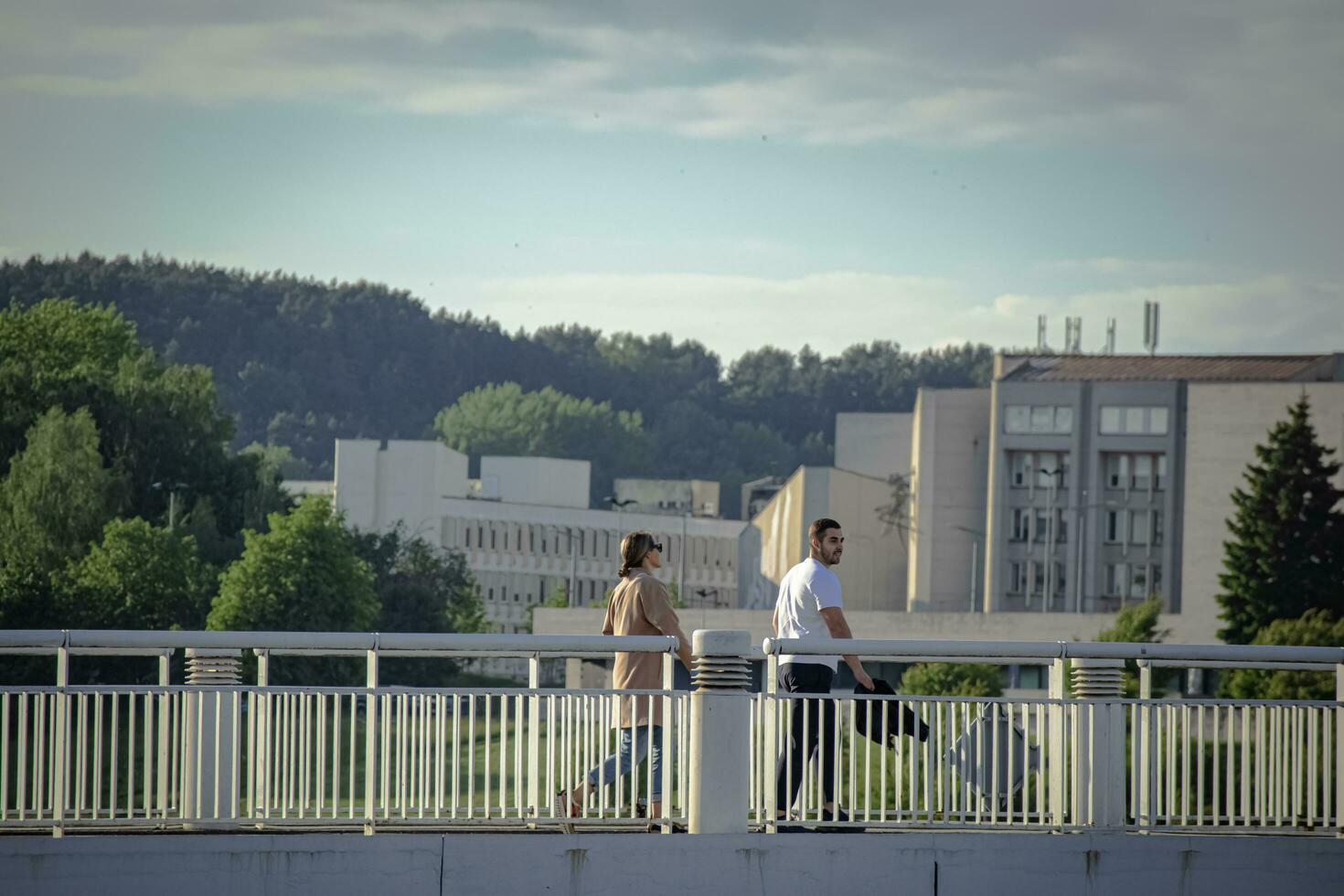 vilnio, Lituania 03 06 2022 giovane donna un uomo a piedi su un' bianca ponte con verde alberi e ufficio edificio su sfondo foto