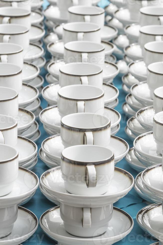 le tazze di caffè bianco con i piatti stanno impilate in fila foto