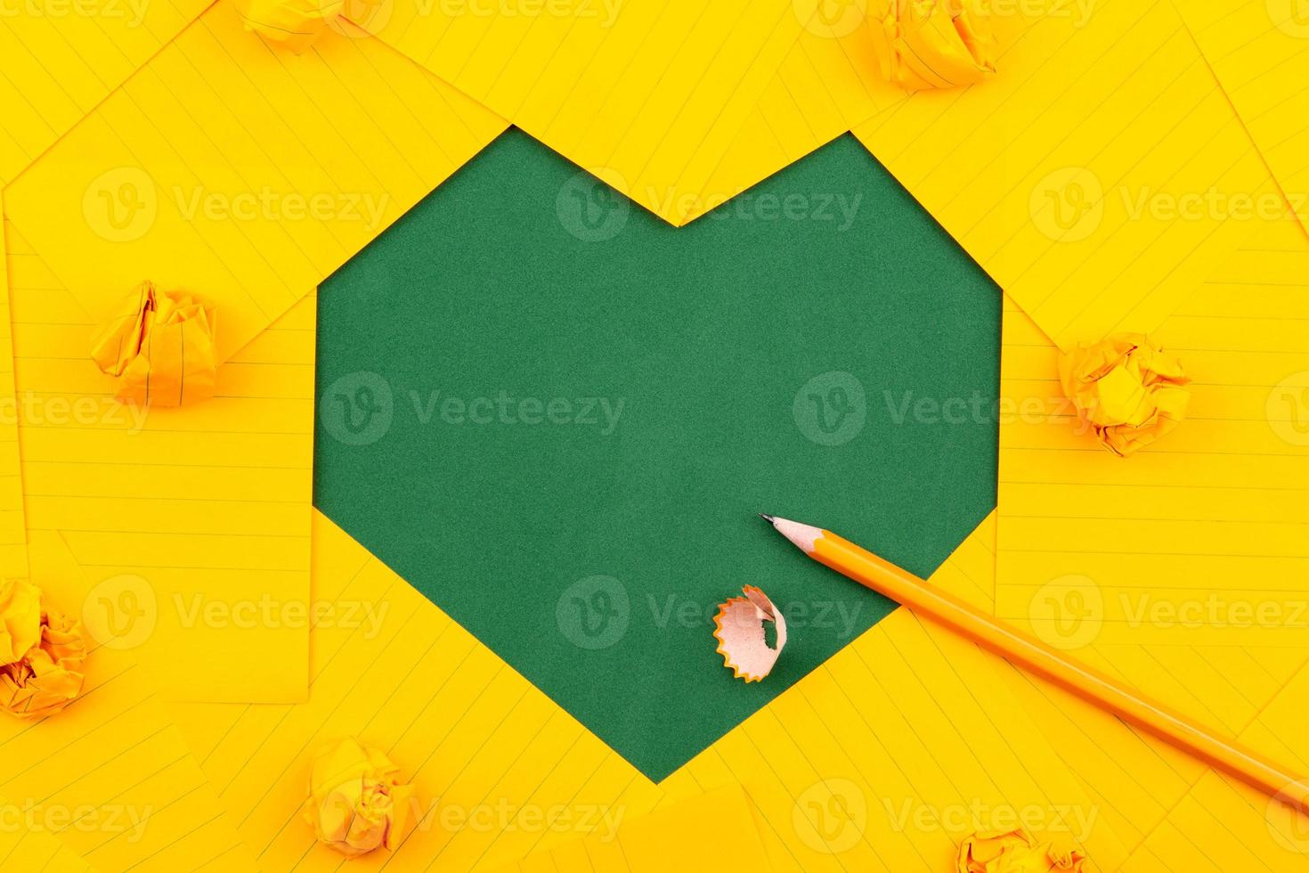 fogli di carta arancione, matita e carta sgualcita su un consiglio scolastico verde a forma di cuore incorniciato foto