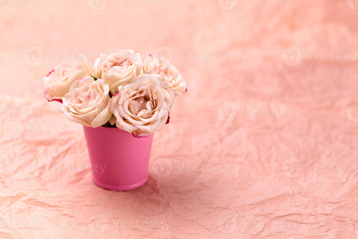 un bouquet di bellissime rose si trova in un piccolo secchio su uno sfondo rosa artigianale con spazio per il testo foto