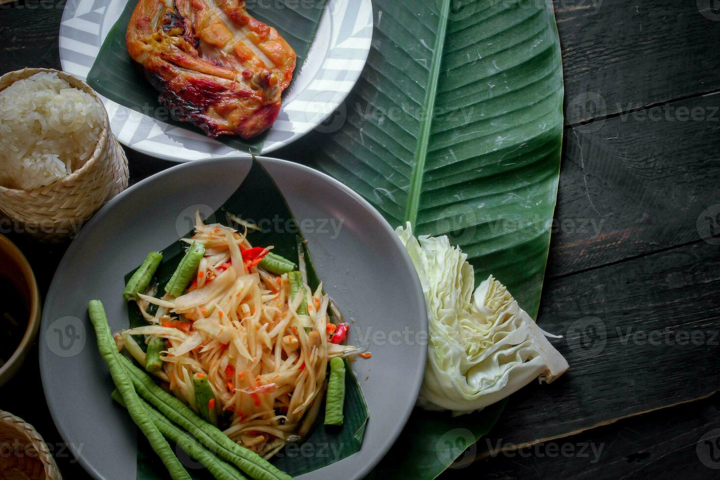 tailandese cibo piatto tutti e due nel Tailandia e Asia papaia insalata o come noi chiamata esso somtum è integrato con grigliato pollo e appiccicoso riso con fresco patatine fritte. servito su il nero di legno tavolo. foto