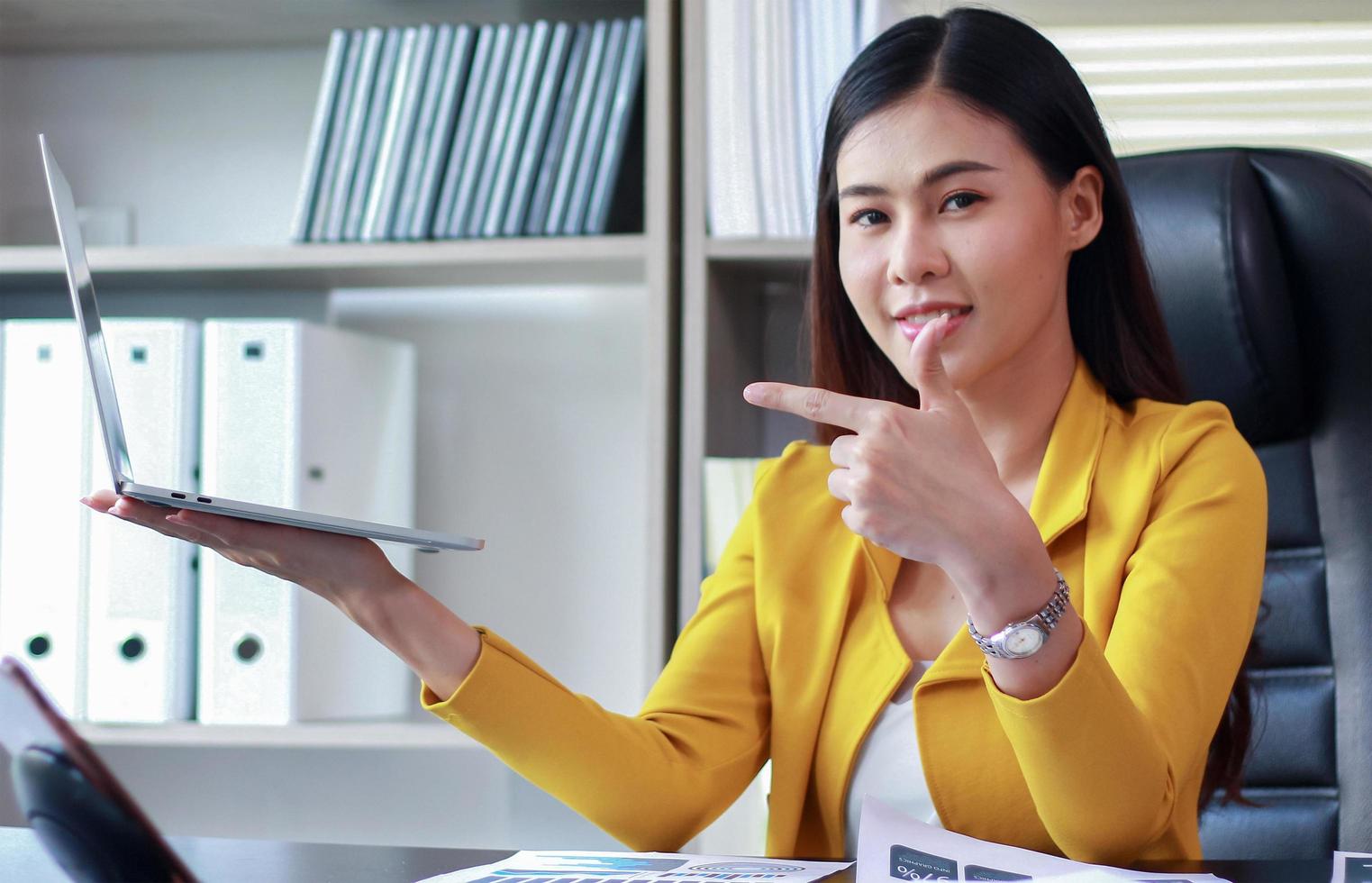 la donna asiatica di affari tiene un computer portatile che si siede nell'ufficio e che sorride felicemente foto