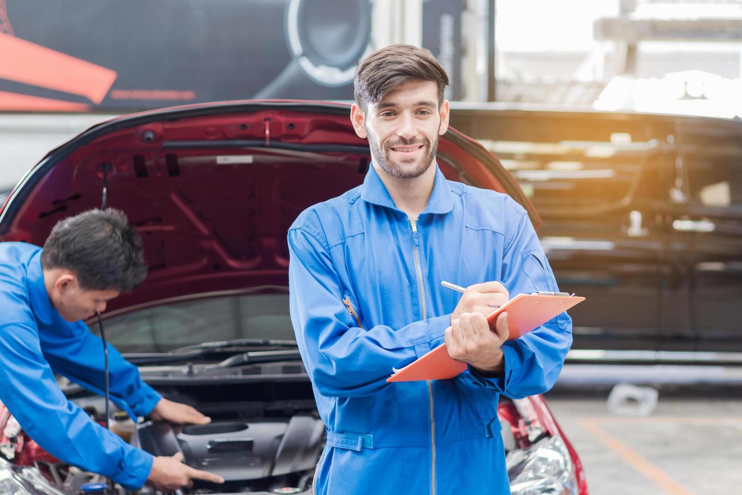 ritratto di un bel giovane tecnico in una veste blu che lavora in un centro di riparazione auto e verifica i dati tecnici foto