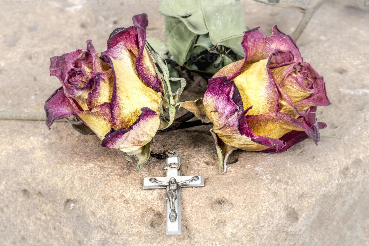 croce cristiana sul rosario e rose rosse gialle secche giacciono su un'arenaria foto