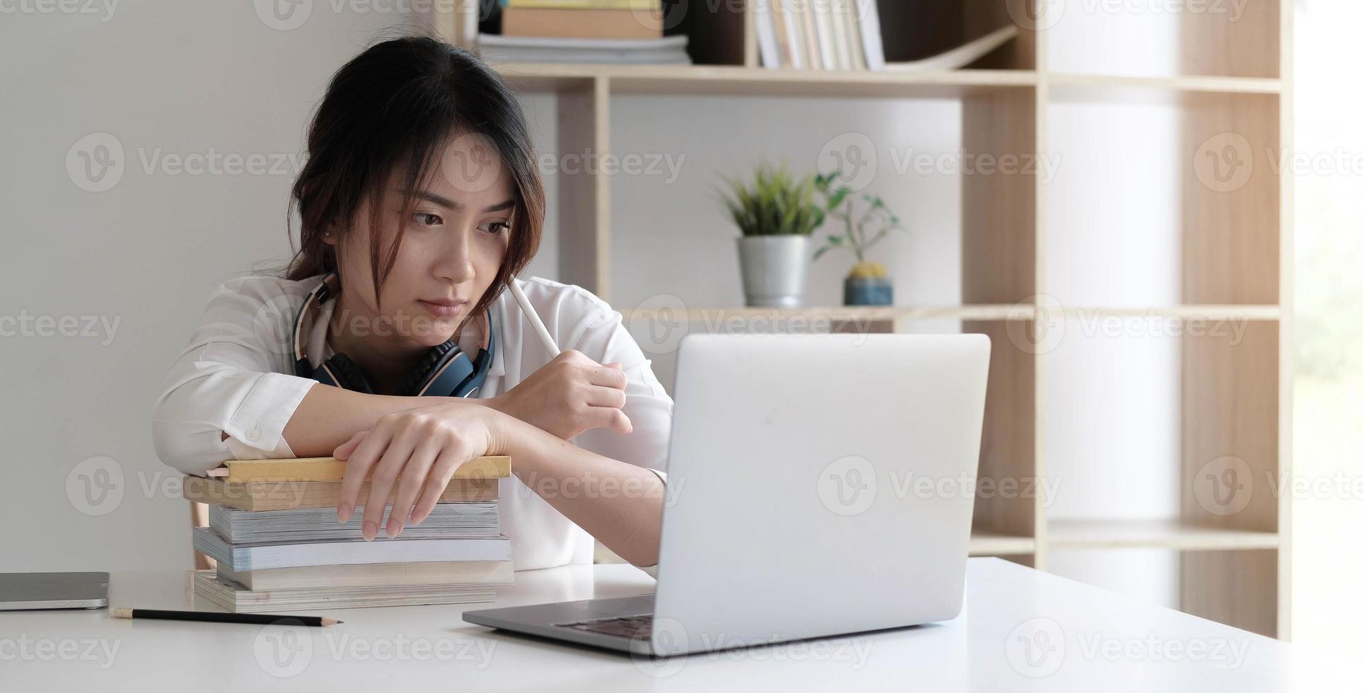 vista frontale sulla giovane donna indoeuropea studio davanti al computer portatile a casa libro di lettura della ragazza preparazione test d'esame con consultazione in linea foto