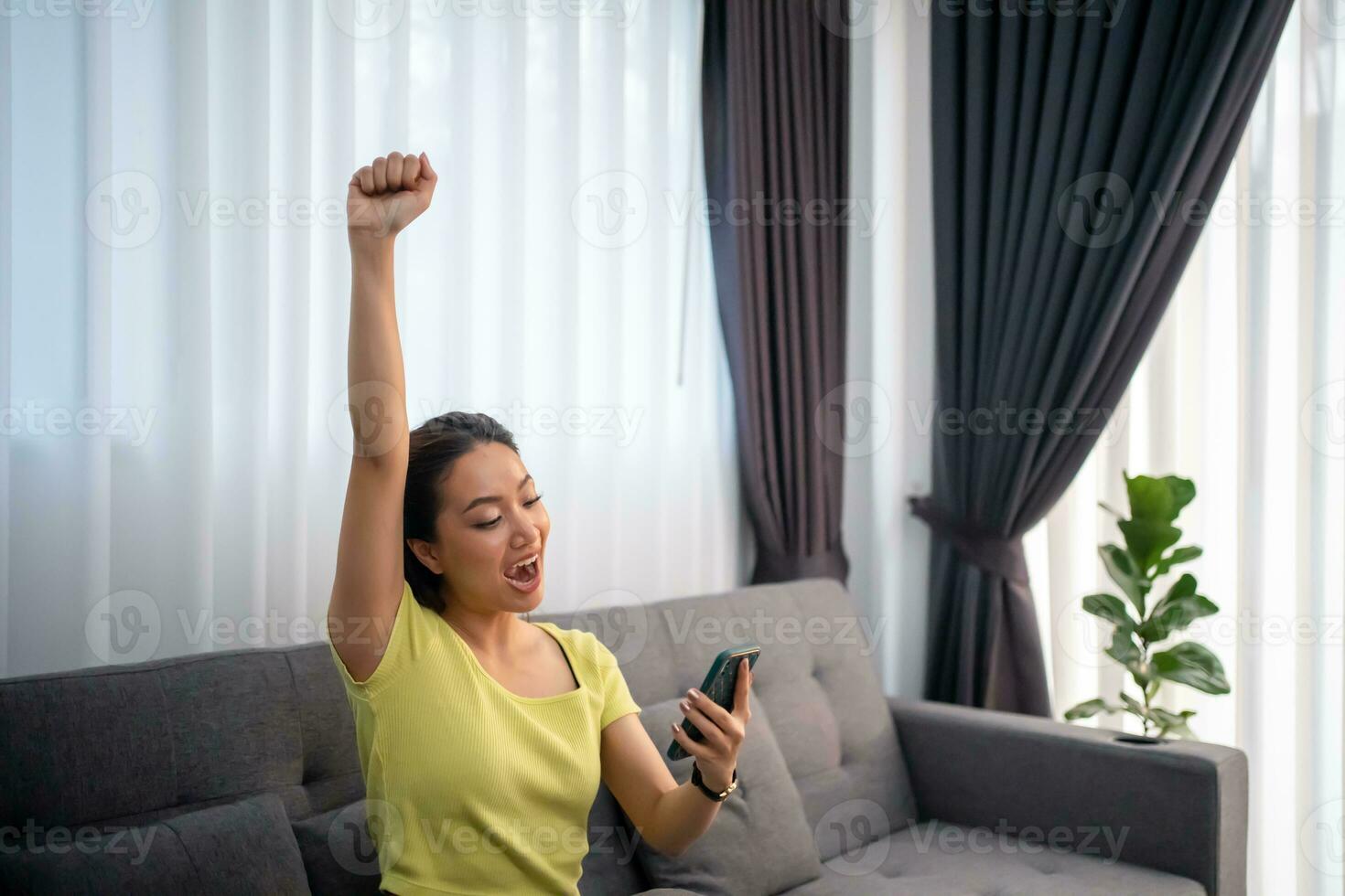 asiatico donna seduta su divano a casa con mobile Telefono e sensazione eccitato e contento. foto