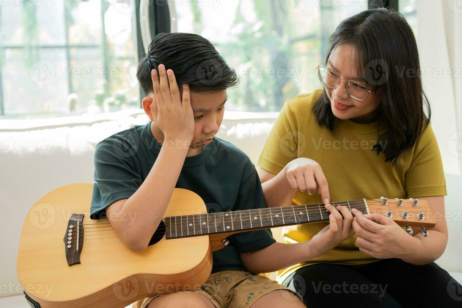 la madre asiatica abbraccia il figlio, il ragazzo asiatico che suona la chitarra e la madre abbraccia sul divano e si sente apprezzata e incoraggiata. concetto di famiglia felice, stile di vita di apprendimento e divertimento, legami familiari d'amore foto