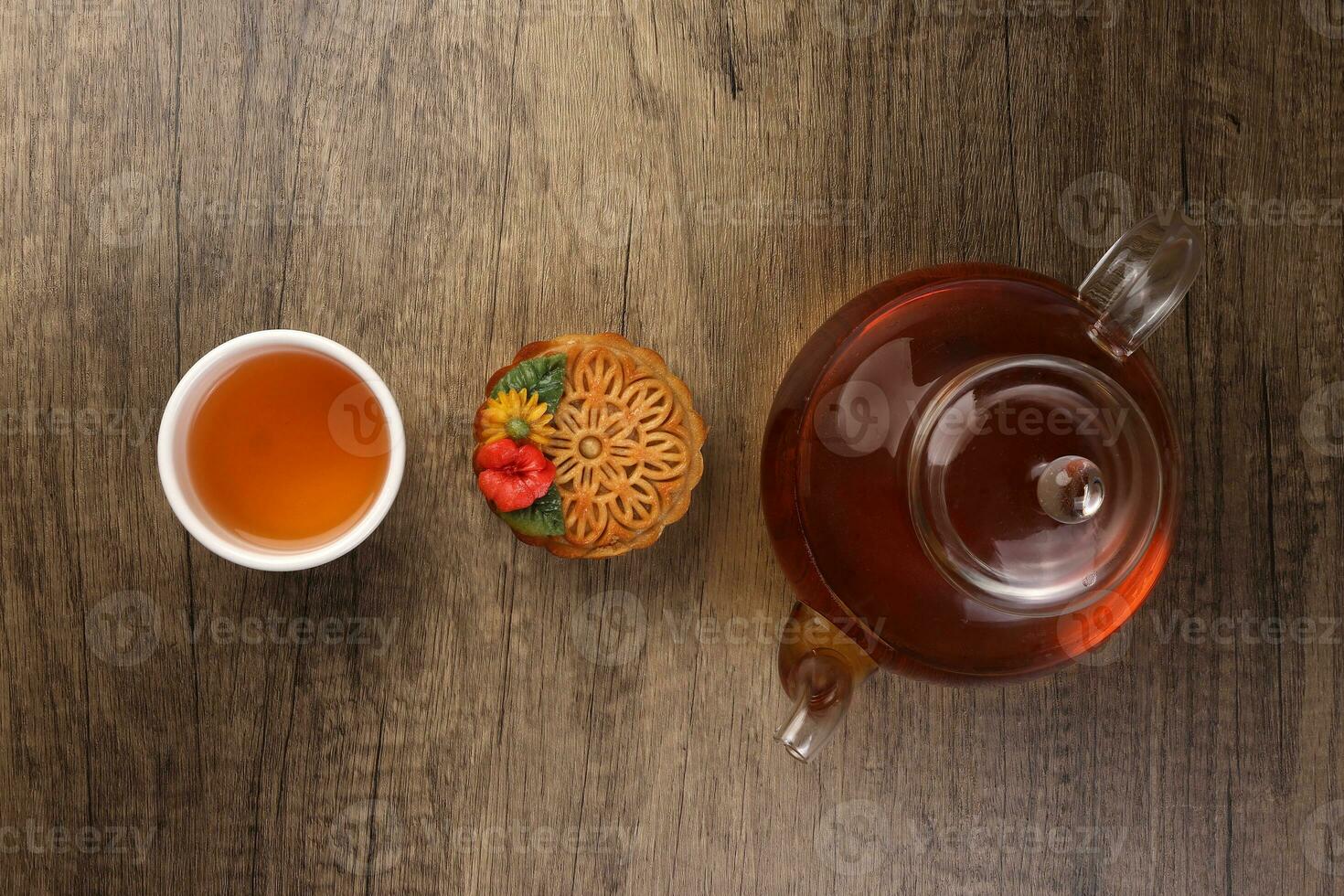 colorato fiore decorato mooncake tagliare fetta metà strato Cinese medio autunno Festival su bicchiere teiera bianca ceramica tazza di tè al di sopra di rustico legna confine foto