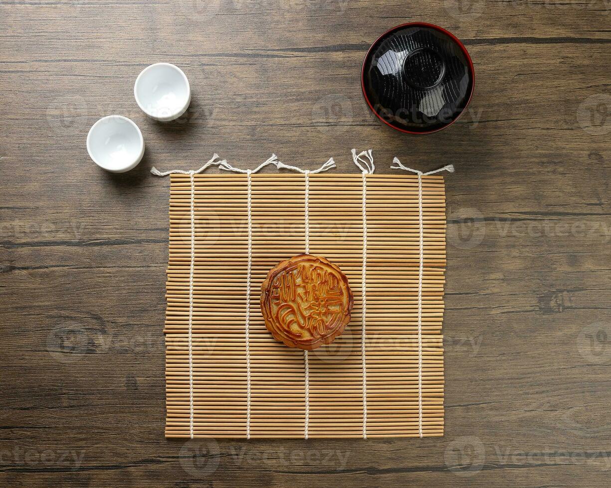 Cinese al forno decorato mooncake medio autunno Festival il giro Luna torta Riempimento regalo desiderio offerta su bambù stuoia al di sopra di di legno tavolo mini tazza foto