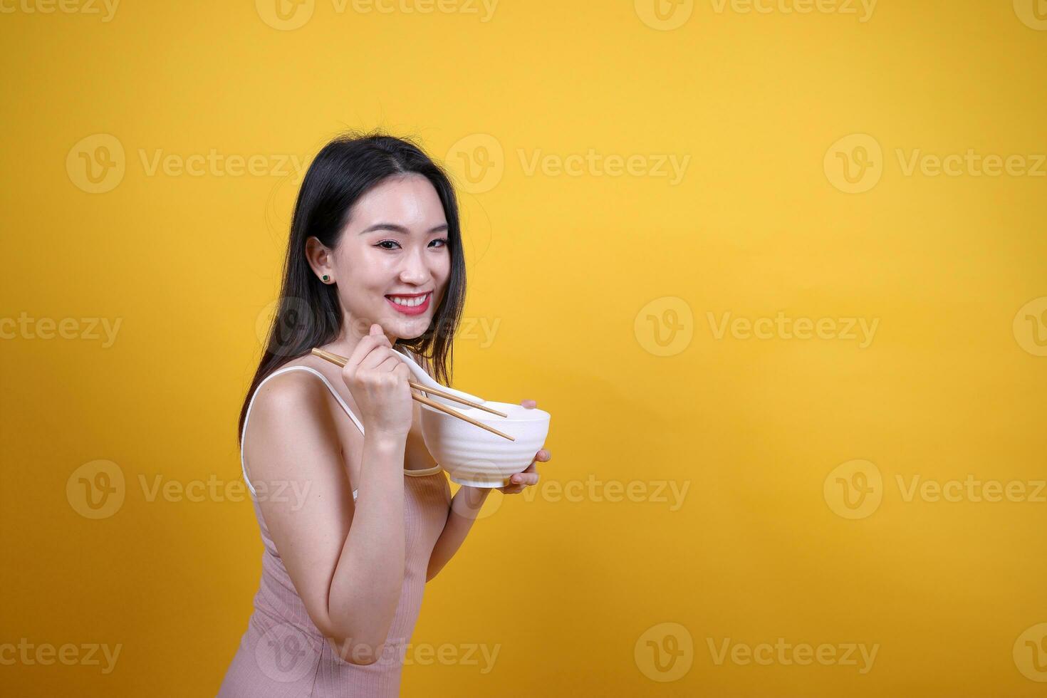 bellissimo giovane Sud est asiatico donna Tenere chines vuoto bacchette Cinese la minestra cucchiaio ciotola utensile fare finta recitazione in posa vedere mangiare gusto odore alimentazione offrire soddisfazione delizioso giallo arancia sfondo foto