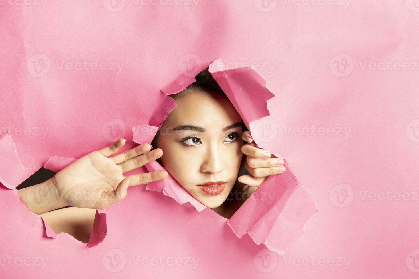 giovane bellissimo asiatico donna espressione attraverso strappato carta buco foto