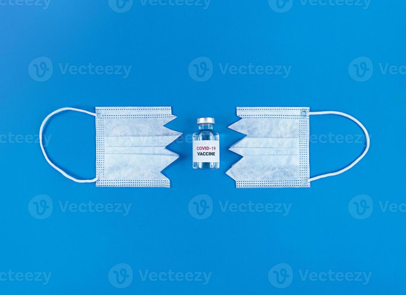 fiala con vaccino covid19 tra due parti di mascherina medica tagliata su sfondo blu foto