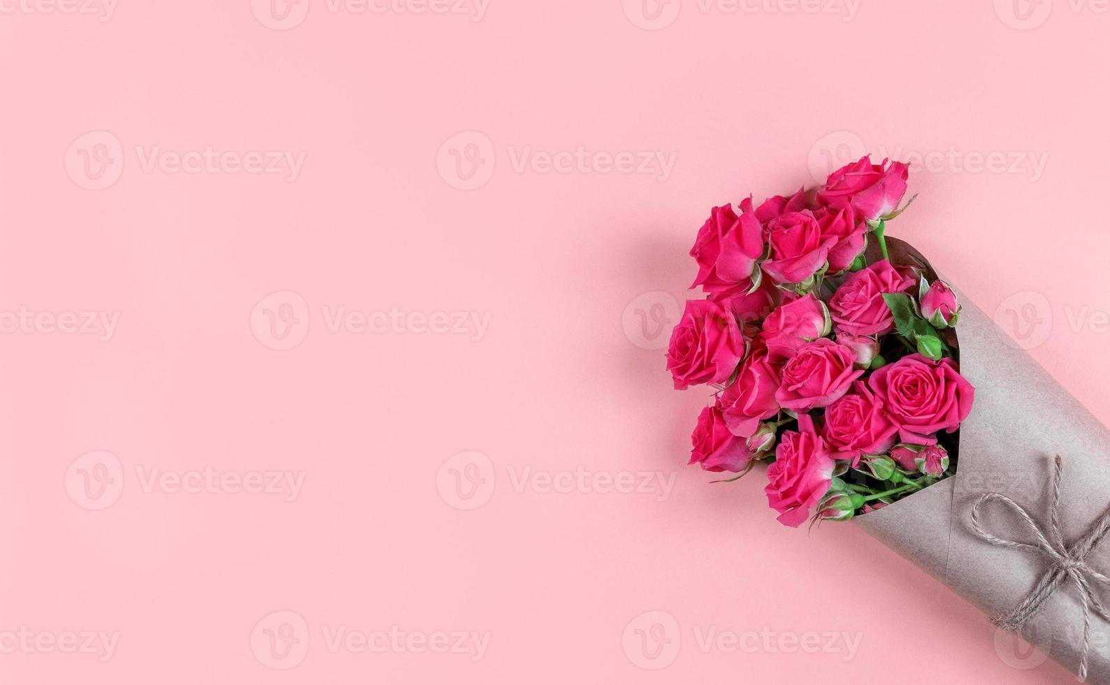 bouquet di piccole rose fiorite avvolte in carta artigianale su sfondo rosa con spazio di copia foto