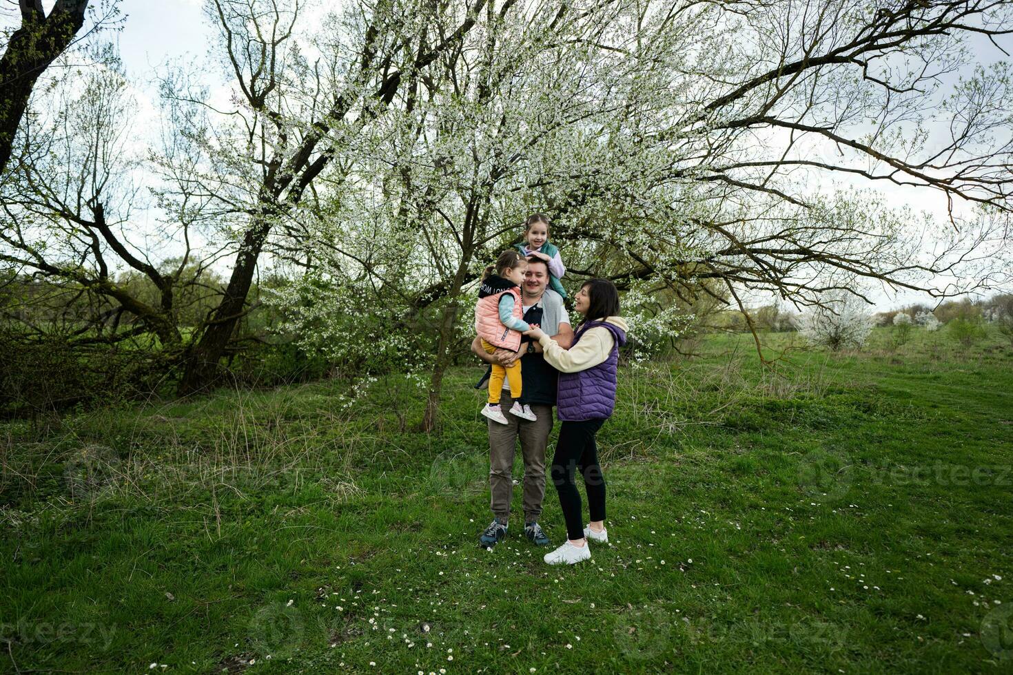 famiglia con Due figlie nel primavera prato su il sfondo di un' fioritura albero. foto