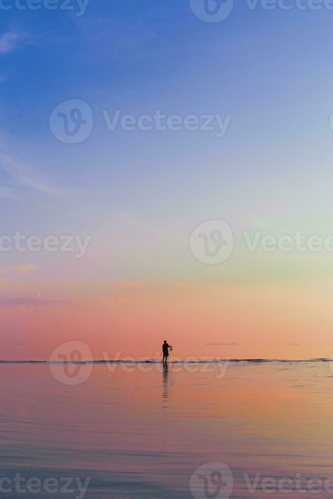 verticale di pescatori attraente pesce nel il mare utilizzando pesca netto a tramonto. foto