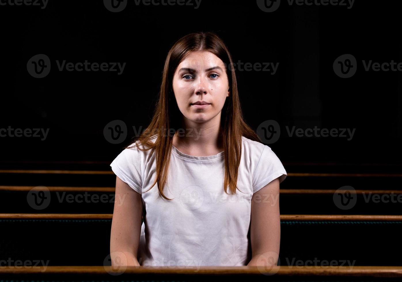 una giovane ragazza è seduta da sola in una grande sala guardando la telecamera foto