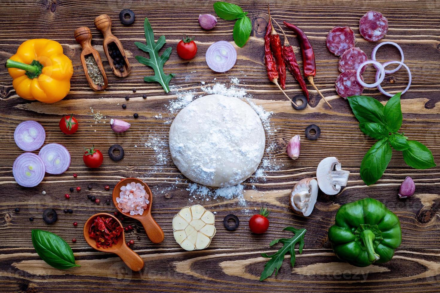 pasta cruda con ingredienti per pizza fatta in casa su fondo di legno squallido foto