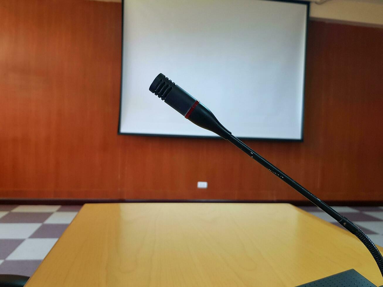 nero microfono su di legno scrivania per parlando o presentazione nel conferenza o incontro camera con bianca proiettore tavola sfocato sfondo. dispositivo e attrezzo foto