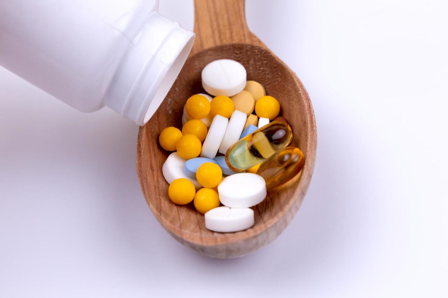 pillole medicinali e farmaci in un cucchiaio di legno su sfondo bianco con spazio di copia foto