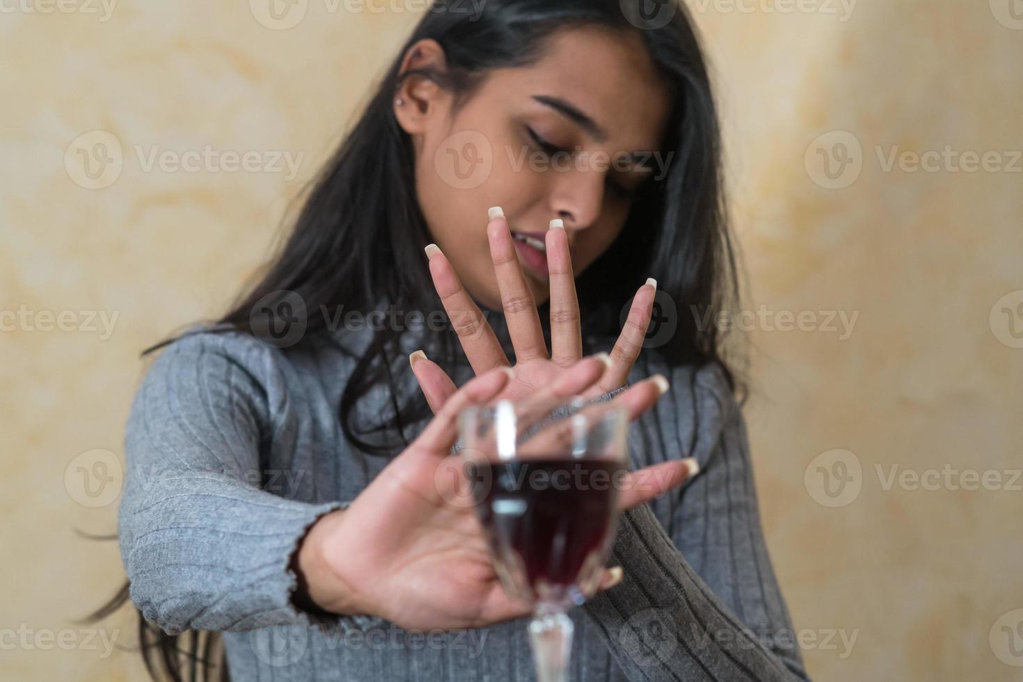 Rinunciando all'alcol una giovane donna al tavolo rifiuta un bicchiere di vino rosso con la mano foto