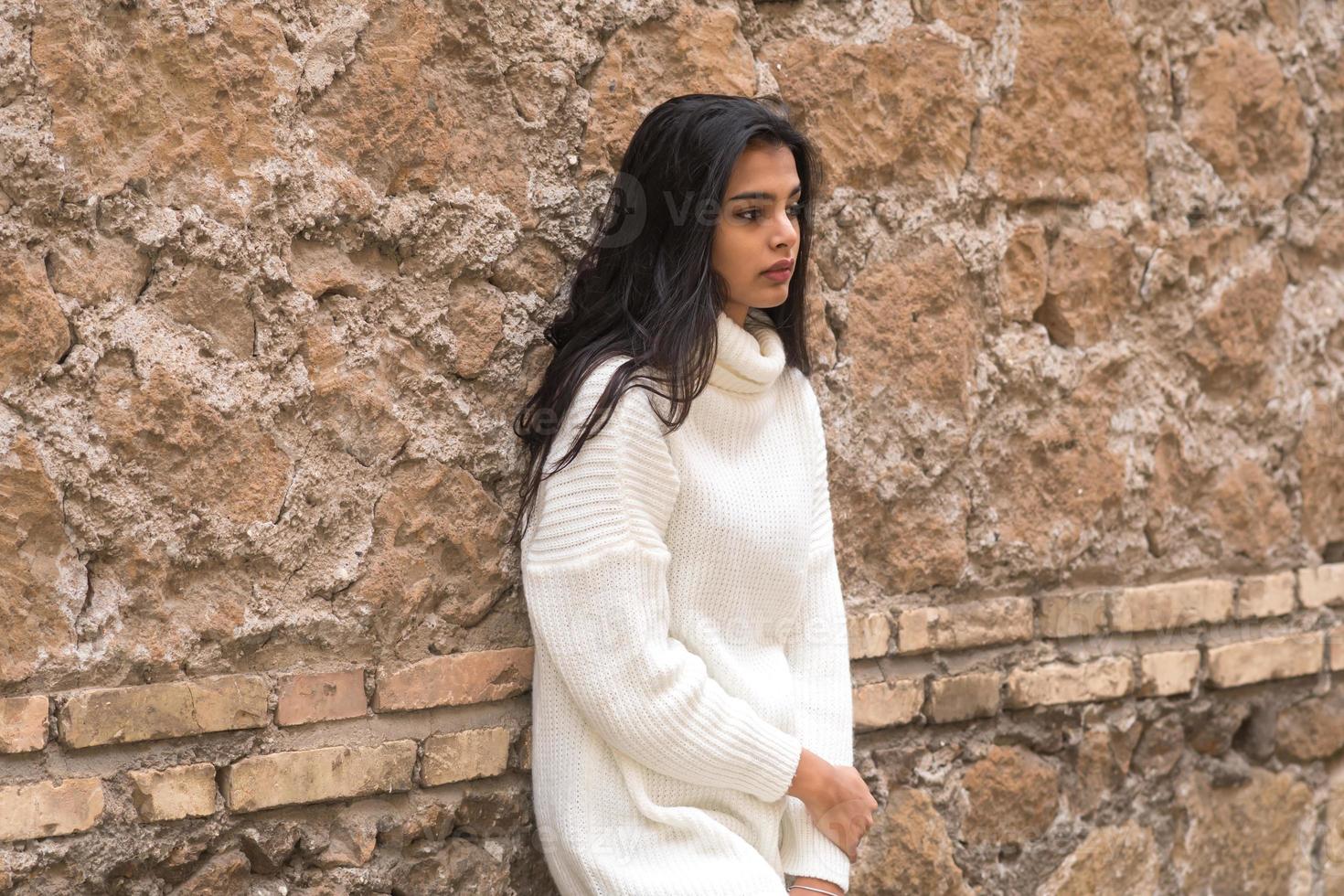 giovane donna bruna contemplativa appoggiata a un muro di mattoni foto