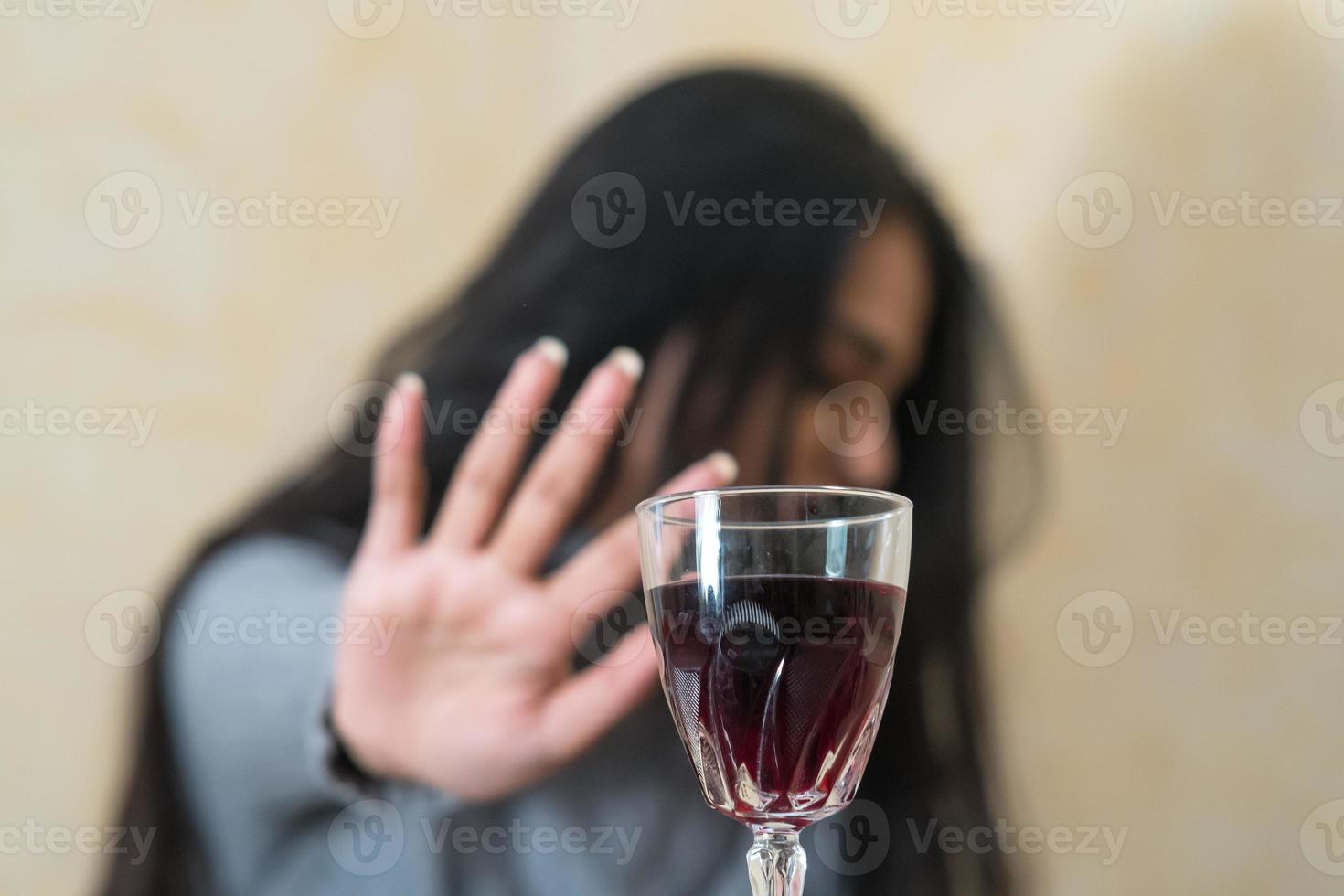 rinunciare all'alcool una giovane donna al tavolo rifiuta con la mano un bicchiere di vino rosso fuoco selettivo foto