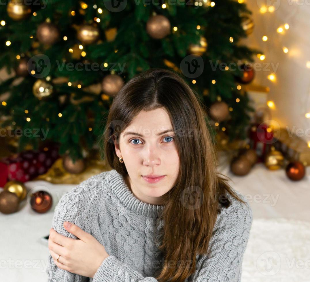 giovane bella donna alla moda in vestito lavorato a maglia grigio vicino all'albero di Natale foto
