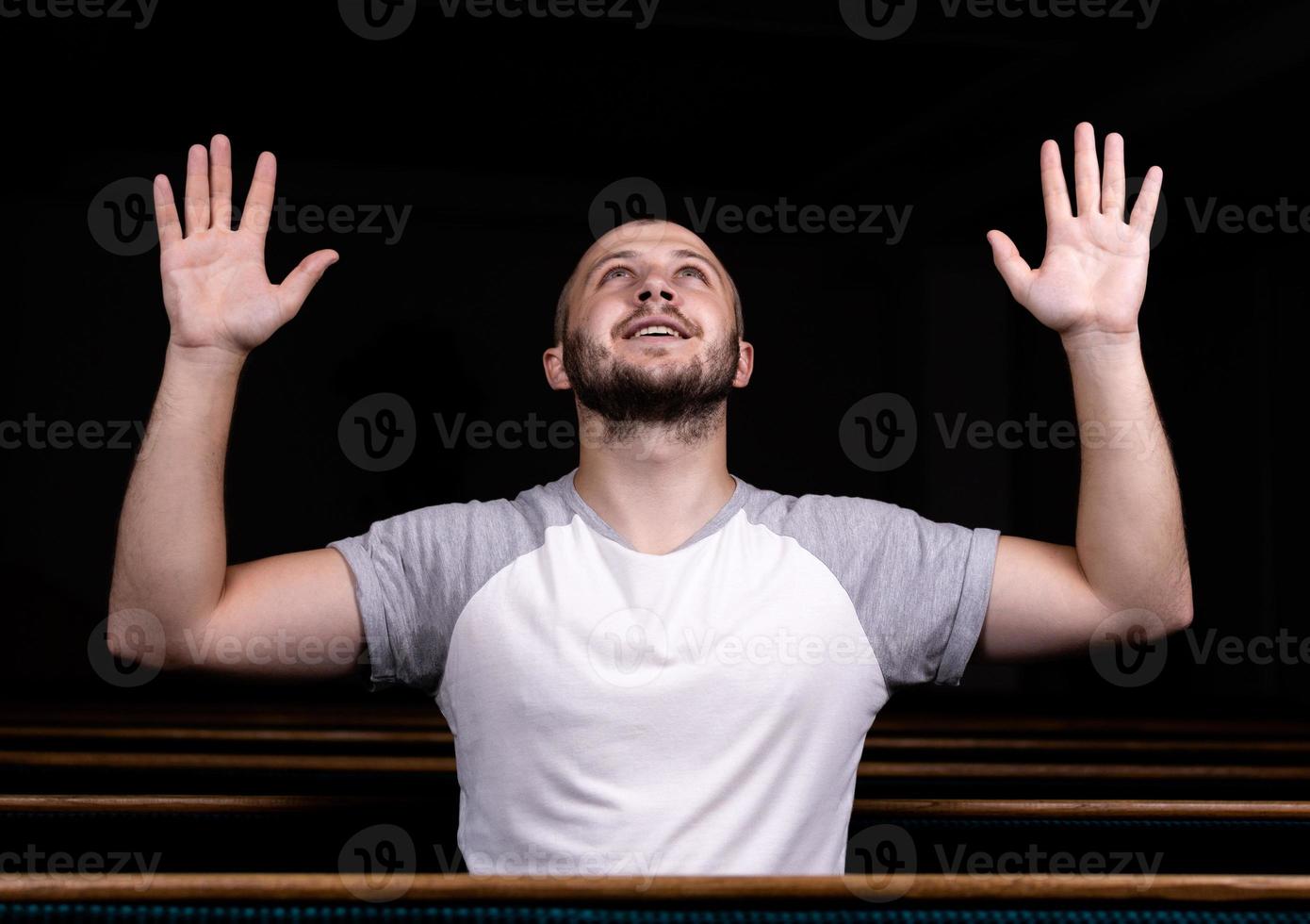 un uomo cristiano in camicia bianca è seduto con le mani in alto e prega con cuore umile nella chiesa foto