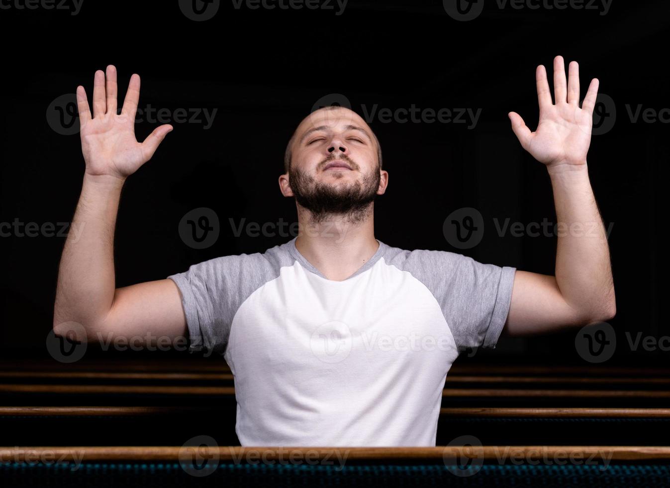 un uomo cristiano in camicia bianca è seduto con le mani in alto e prega con cuore umile nella chiesa foto