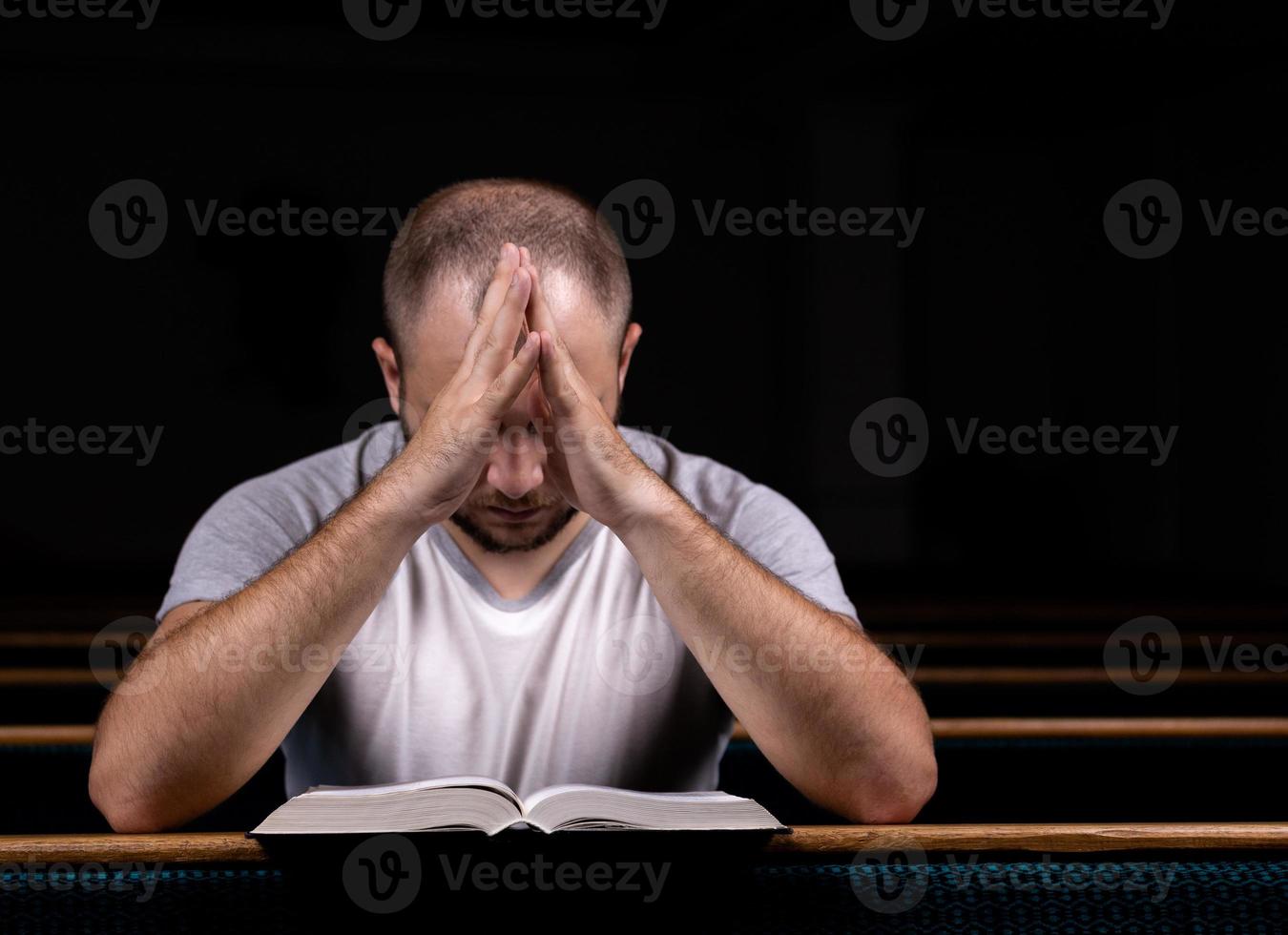 un giovane ragazzo seduto su una panchina della chiesa legge la Bibbia e prega foto