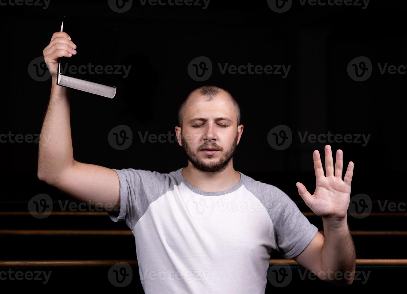 un giovane ragazzo seduto su una panchina della chiesa legge la Bibbia e prega foto