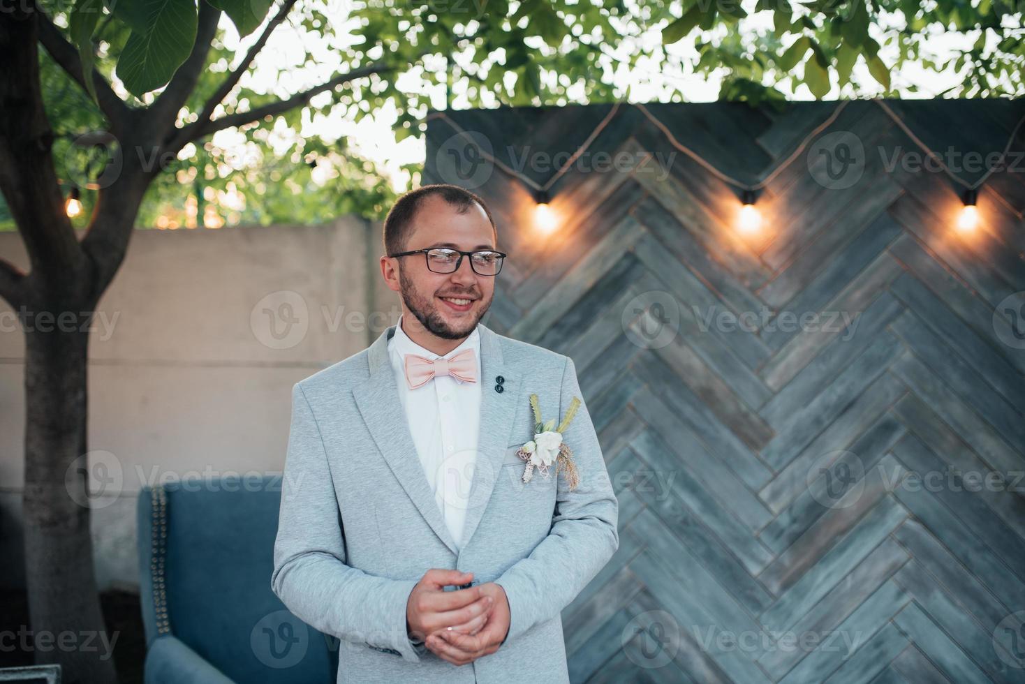 foto di matrimonio di emozioni di uno sposo barbuto con gli occhiali in una giacca grigia e in stile rustico